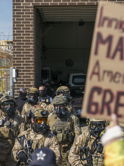 Heavily armed ICE and Border Patrol agents guard the Broadview ICE facility from peaceful protesters opposed to 'Operation Midway Blitz' in Chicagoland; their sign reads 'Immigrants Make America Great'