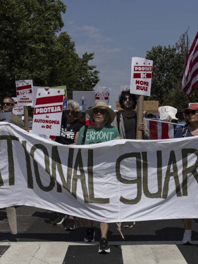 Demonstrators march in Washington, DC carrying a banner that reads " NO NATIONAL GUARD IN DC".