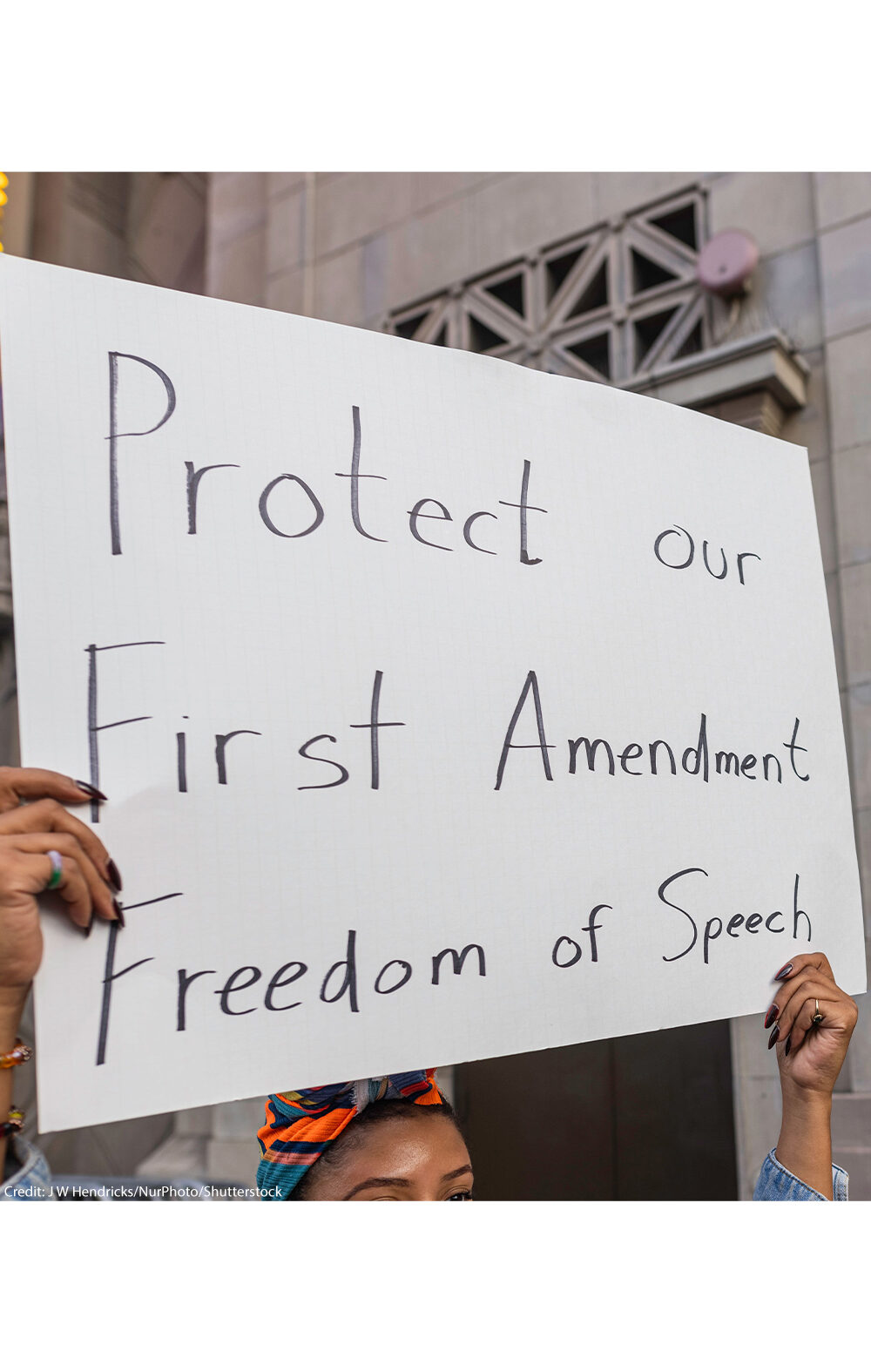 A person holds a large handwritten sign reading “Protect our First Amendment Freedom of Speech” during a protest outside the El Capitan Entertainment Centre, where Jimmy Kimmel Live! is filmed. Behind them, another protester in a skeleton costume holds a cardboard sign depicting a crossed-out image of Jimmy Kimmel. The demonstration is in response to ABC’s decision to pull Kimmel off the air following his remarks about Charlie Kirk.