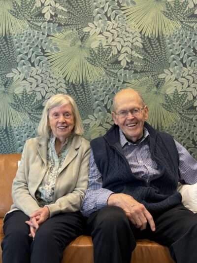 Laurie and Richard Eckman are sitting close to each other on a couch and smiling.