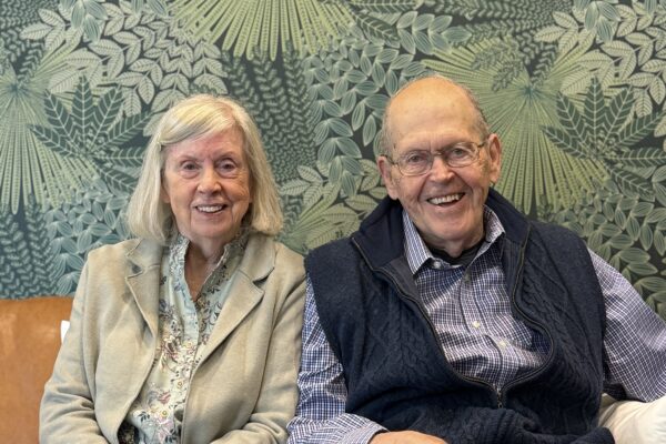 Laurie and Richard Eckman are sitting close to each other on a couch and smiling.