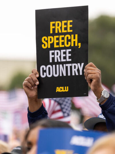 A protestor holds a sign that says Free Speech, Free Country