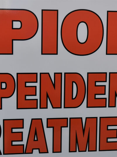 Close-up of a sign reading “OPIOID DEPENDENCE TREATMENT” in large red letters on a white background.