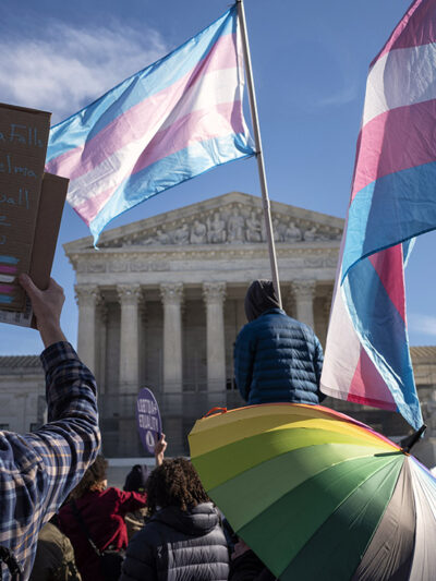 A group of demonstrators, in front of the Supreme Court, some of which hold transgender flags.