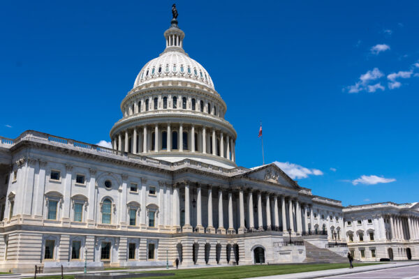 Wide daytime view of the U.S. Capitol building in Washington, D.C., with the white dome and columns under a bright blue sky.