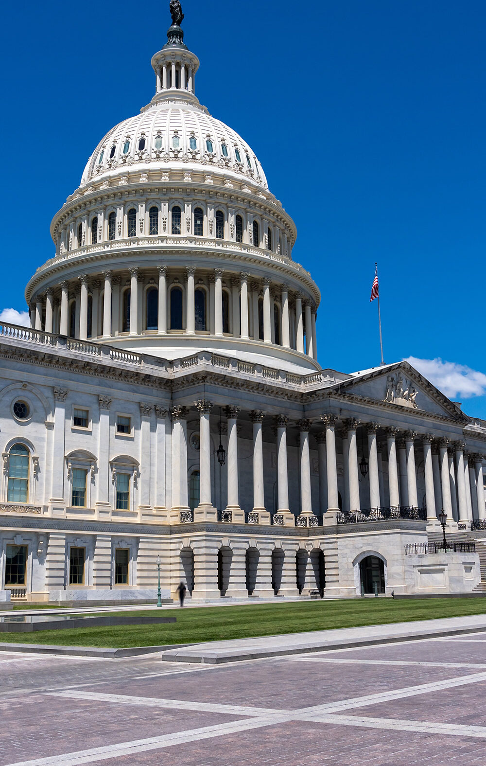 Wide daytime view of the U.S. Capitol building in Washington, D.C., with the white dome and columns under a bright blue sky.