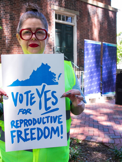 A photo of Heather St. Amand holding a sign that says "Vote Yes on Reproductive Freedom."