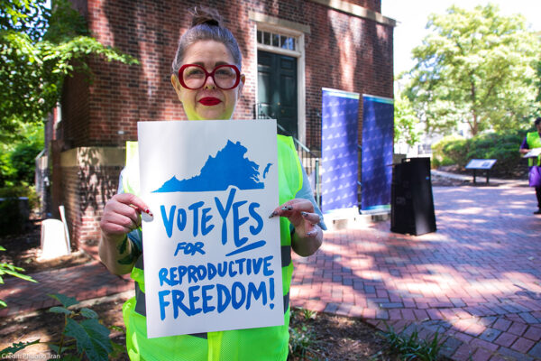 A photo of Heather St. Amand holding a sign that says "Vote Yes on Reproductive Freedom."