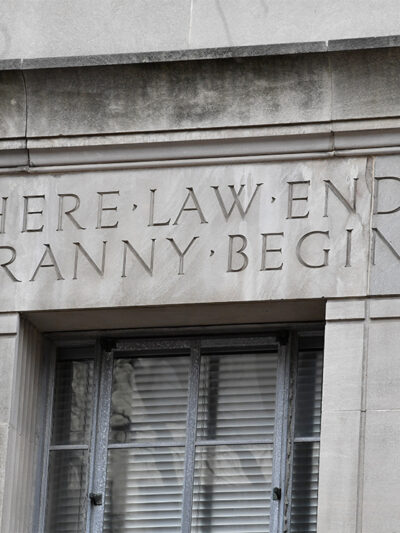 Engraved words on the facade of the U.S. Department of Justice building read "WHERE LAW ENDS TYRANNY BEGINS," above a window set into the stone exterior.