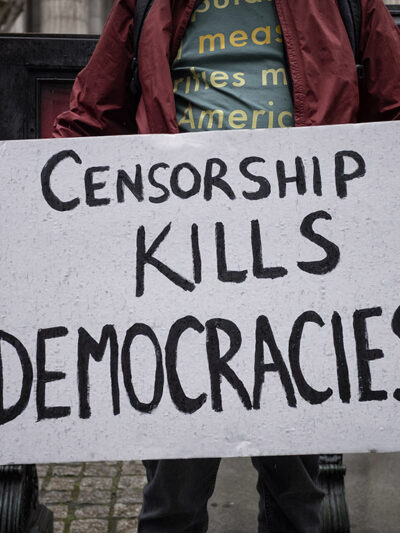 A demonstrator holding a sign that says "Censorship Kills Democracies."