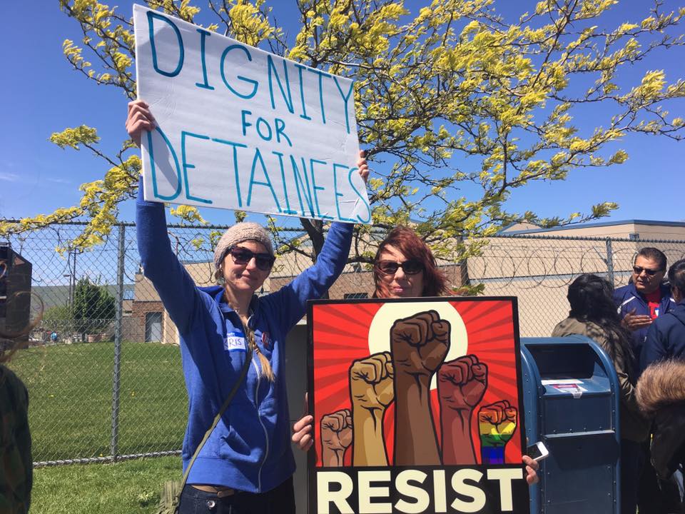 protesters hold signs saying "dignity for detainees" and "resist"
