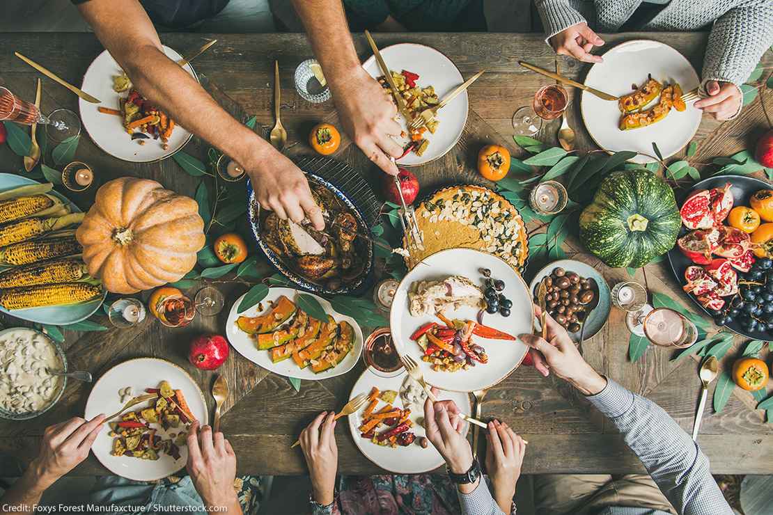 Flat-lay of friends feasting at Thanksgiving Day table with turkey, pumpkin pie, roasted seasonal vegetables and fruit, top view