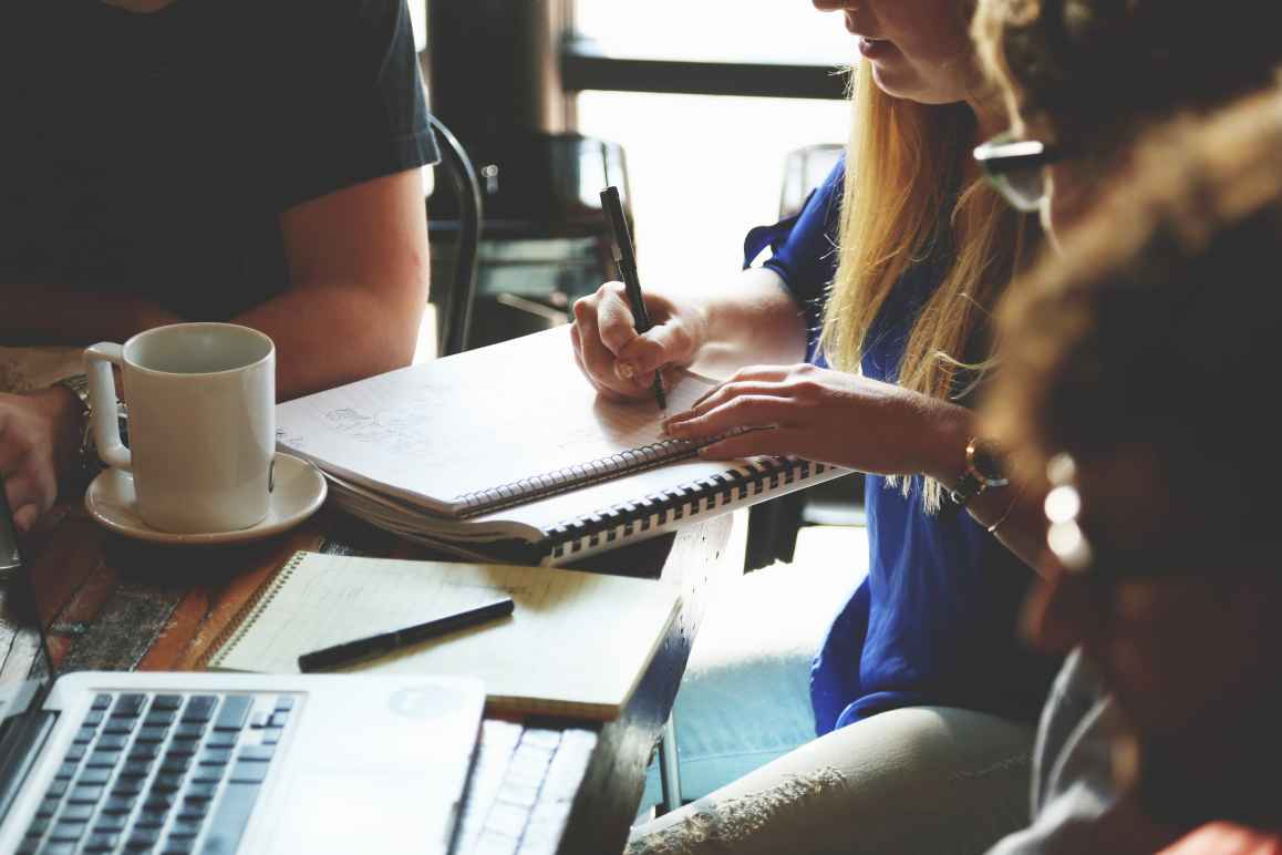 Four people sit at a table with a computer and notebooks