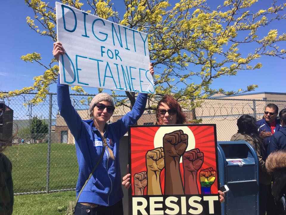 protesters hold signs saying "dignity for detainees" and "resist"
