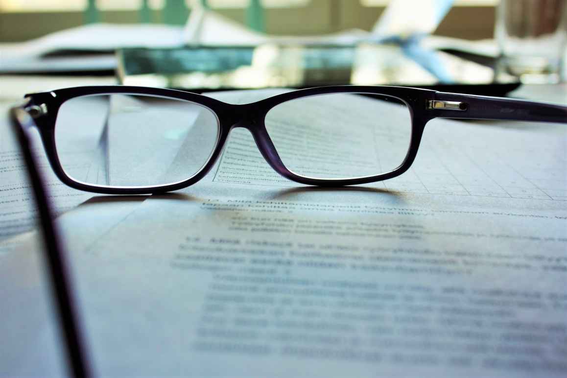 A pair of reading glasses rests on a document, whose content is indistinguishable 