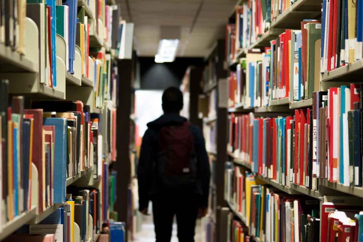A student walks through shelves of books in a school library