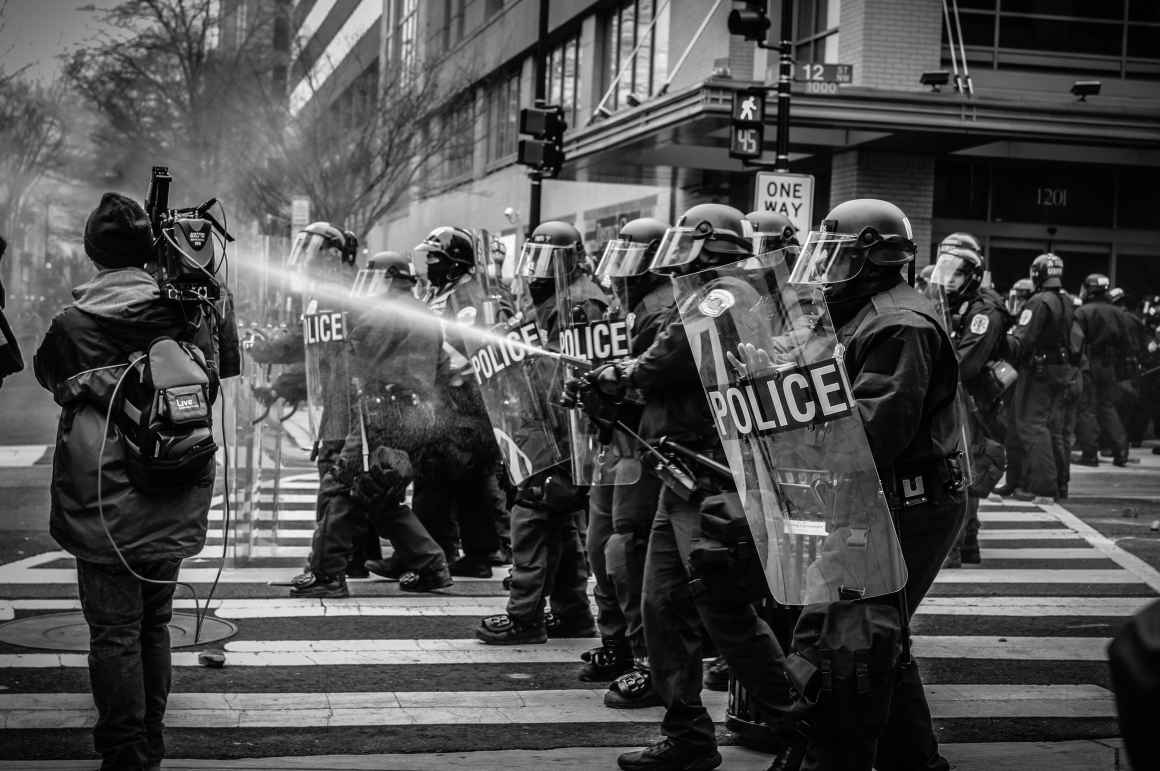 Police in riot gear spray a protester with water