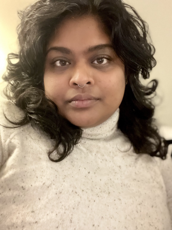 Stacie Balkaran (she/they), a person with brown skin and long curly dark hair, wearing a turtleneck