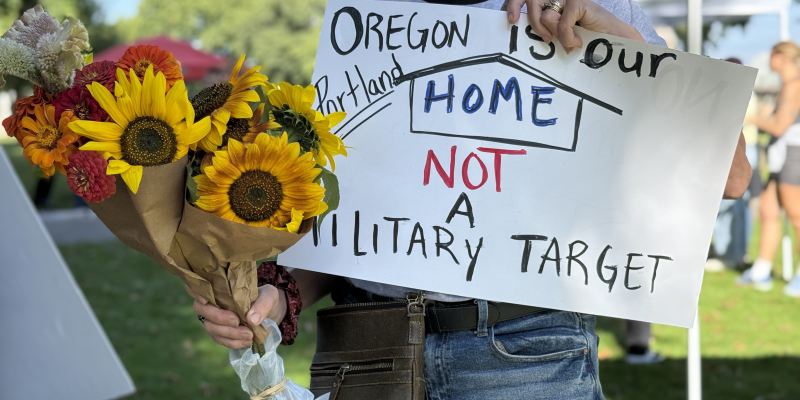 Rally attendee with flowers and a poster that reads Oregon is Not a Military Target