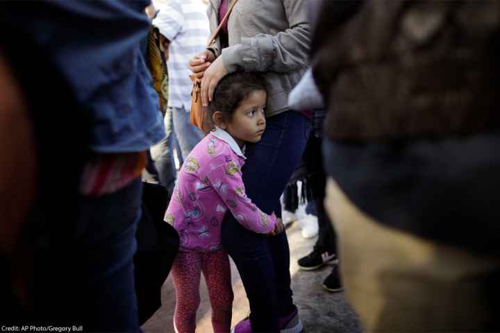A young child holds on to her mother legs as they wait with other families to request political asylum in the United States, across the border in Tijuana, Mexico.