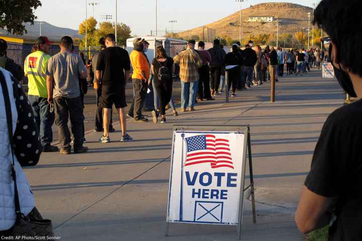A sign that says "vote here" among a line of voters.