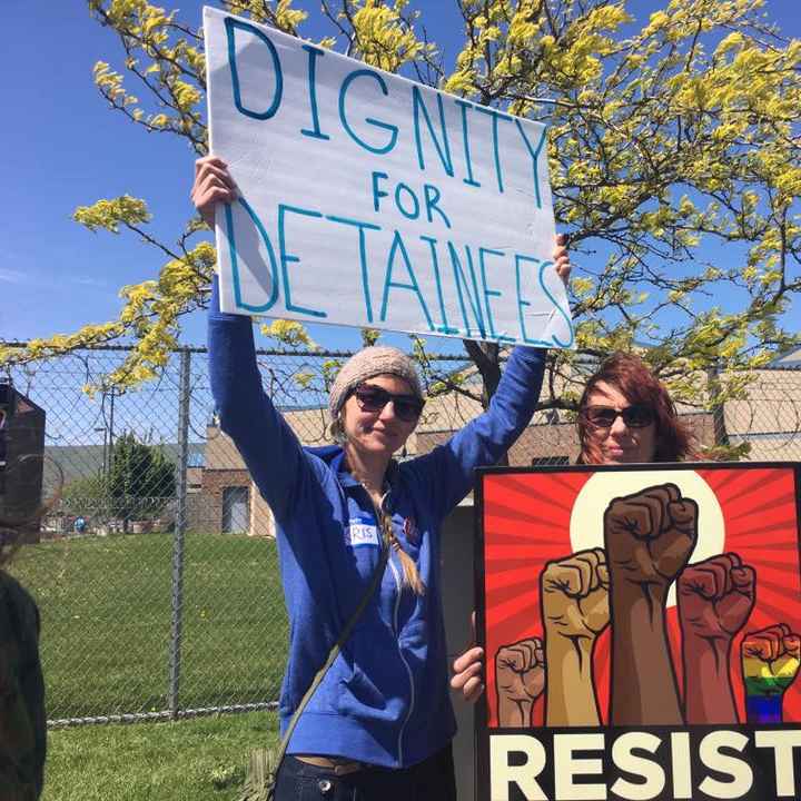 protesters hold signs saying "dignity for detainees" and "resist"