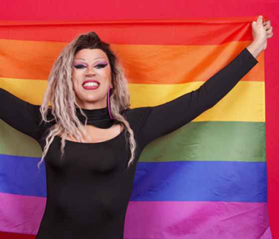 A drag queen holds up a rainbow flag with pride. Show your support by donating to the Drag Defense Fund to protect this freedom of expression.