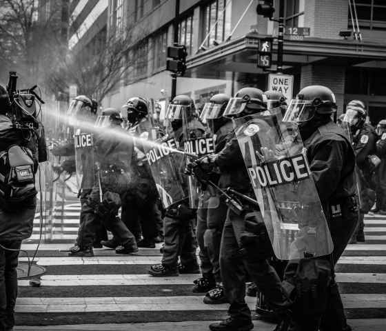 Police in riot gear spray a protester with water